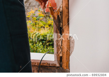 The man with a hand saw cuts the mounting wool around the window frame, installation of an old wooden window, window replacement. 69932804