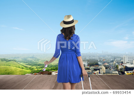 Asian woman with a suitcase looking at green landscapes and a city Asian woman with a suitcase looking at green landscapes and a city 69933454