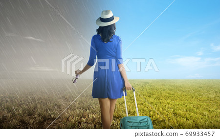 Asian woman with suitcase standing on the meadow Asian woman with suitcase standing on the meadow 69933457