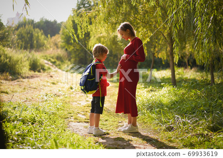 Small boy touching belly of his pregnant mother outdoors. 69933619