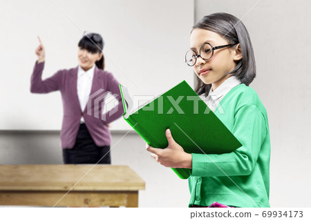 Asian little girl standing and reading the book in the classroom 69934173