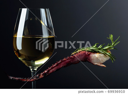 Grilled octopus and white wine glass on a black background. Grilled octopus and white wine glass on a black background. 69936910
