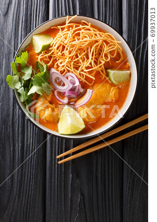 Khao Soi is a popular coconut curry noodles soup with chicken closeup in the bowl. Vertical top view 69937013