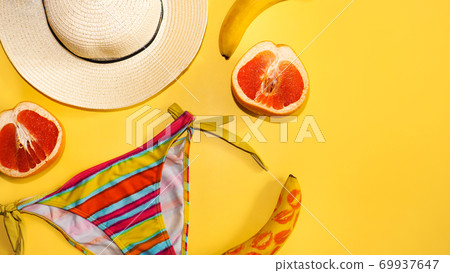 Grapefruit, banana, traw hat and a bright swimsuit on a yellow background 69937647