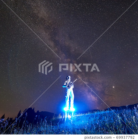 Astronaut playing guitar under beautiful night sky. 69937792