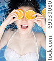 Asian woman is swimming with a slice of orange floating above the water in a blue pool and enjoying a hot summer day. beauty concept. 69939080