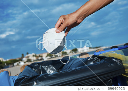 man throws used mask to the trash can on the beach 69940923