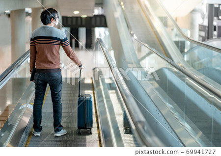 Male tourist carrying suitcase luggage on travelator Male tourist carrying suitcase luggage on travelator 69941727
