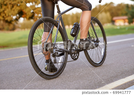 Biking outdoors. Cropped shot of a man cycling outdoors, standing with his bycicle on the road. Focus on male legs Biking outdoors. Cropped shot of a man cycling outdoors, standing with his bycicle on the road. Focus on male legs 69941777