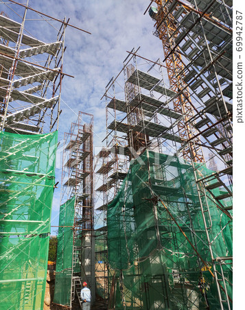 SELANGOR, MALAYSIA -AUGUST 4, 2020: Temporary stairs and scaffolding are used in the construction of high concrete columns. Scaffolding is wrapped with safety netting for safety purposes. SELANGOR, MALAYSIA -AUGUST 4, 2020: Temporary stairs and scaffolding are used in the construction of high concrete columns. Scaffolding is wrapped with safety netting for safety purposes. 69942787