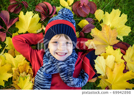 Little kid boy lying in autumn leaves in red pullover. Happy child having fun in autumn park on warm day. Cute school boy smiling and laughing. 69942898