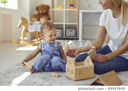 Joyful young nanny and little kid playing with wooden blocks in cozy nursery room 69943649