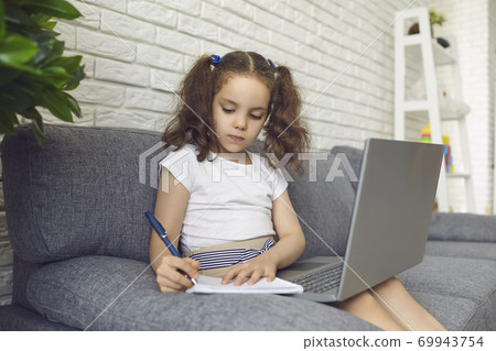 Online education kid. Child in headphones watching video lesson on laptop and taking notes at home Online education kid. Child in headphones watching video lesson on laptop and taking notes at home 69943754