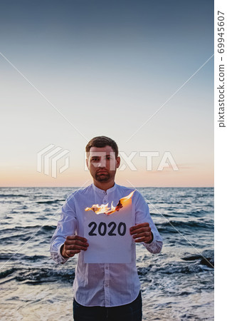 Man holding paper that burns with text 2020 written on it. Man holding paper that burns with text 2020 written on it. 69945607