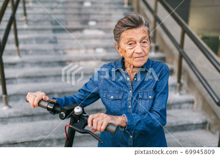 Old woman near scooter. Grandmother progressive woman. Senior having fun. Old woman enjoying her hobbies. Retired lady using modern clean transport. New generation. Mature woman loving her e scooter 69945809