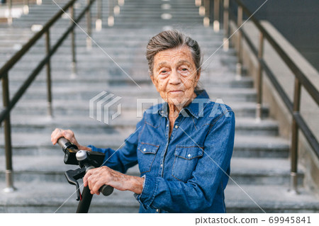90 year old woman with gray hair, wrinkles, progressive and active uses modern electric transport scooter. Lady pensioner use eco friendly city vehicle. Senior female using urban personal transport 69945841