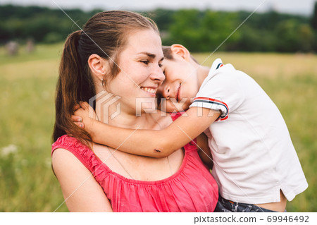 Mother and son hugging in field. Happy mother embracing her son in park. Mother hugging her child. Motherhood. Young mother cuddle her happy baby in fields at sunset. Lovely little kid 69946492