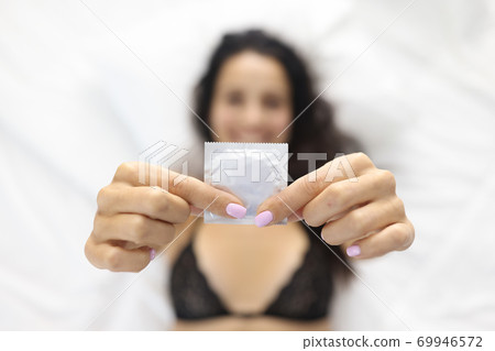 Woman holding condom while lying in bed. Woman holding condom while lying in bed. 69946572
