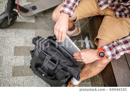 Handsome hipster style bearded man works online freelancer, pulls out laptop with backpack and electric scooter, active lifestyle, backpacker traveler. Ecology and clean ecological mode of transport 69946585