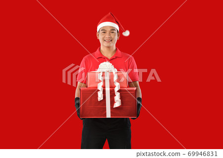 Delivery man in red uniform, face mask, protective gloves, Christmas hat carry boxes of presents Delivery man in red uniform, face mask, protective gloves, Christmas hat carry boxes of presents 69946831