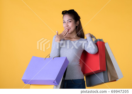 Young Asian woman with colourful shopping bags and credit card isolated on yellow background Young Asian woman with colourful shopping bags and credit card isolated on yellow background 69947205