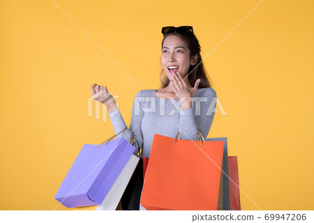 Young Asian woman with colourful shopping bags and credit card isolated on yellow background Young Asian woman with colourful shopping bags and credit card isolated on yellow background 69947206