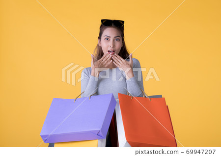 Young Asian woman with colourful shopping bags and credit card isolated on yellow background Young Asian woman with colourful shopping bags and credit card isolated on yellow background 69947207