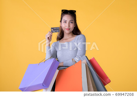 Young Asian woman with colourful shopping bags and credit card isolated on yellow background Young Asian woman with colourful shopping bags and credit card isolated on yellow background 69947208