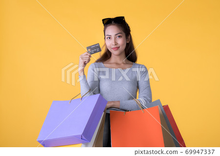 Young Asian woman with colourful shopping bags and credit card isolated on yellow background 69947337