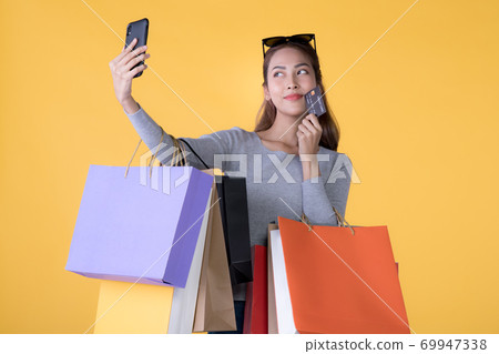 Asian woman with shopping bags, credit card and taking selfie with smartphone isolated on yellow  69947338