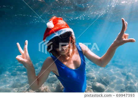 Happy freediver woman with New year cap glides underwater in blue ocean. Christmas holidays concept Happy freediver woman with New year cap glides underwater in blue ocean. Christmas holidays concept 69947393
