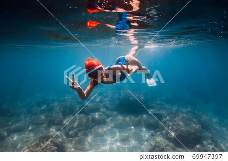 Happy freediver woman with New year cap glides underwater in blue ocean. Christmas holidays concept Happy freediver woman with New year cap glides underwater in blue ocean. Christmas holidays concept 69947397
