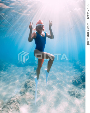 Happy freediver woman with New year cap glides underwater in blue ocean. Christmas holidays concept Happy freediver woman with New year cap glides underwater in blue ocean. Christmas holidays concept 69947400