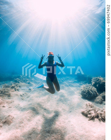 Happy freediver woman with New year cap glides underwater in blue ocean. Christmas holidays concept Happy freediver woman with New year cap glides underwater in blue ocean. Christmas holidays concept 69947402