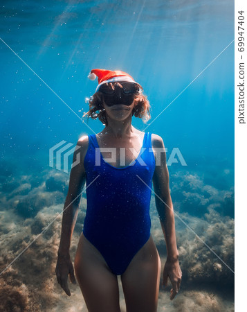 Happy freediver woman with New year cap glides underwater in blue ocean. Christmas holidays concept Happy freediver woman with New year cap glides underwater in blue ocean. Christmas holidays concept 69947404