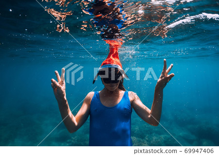 Happy freediver woman with New year cap glides underwater in blue ocean. Christmas holidays concept Happy freediver woman with New year cap glides underwater in blue ocean. Christmas holidays concept 69947406