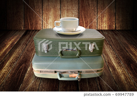 Coffee cup on vintage travel bag with wooden wall background Coffee cup on vintage travel bag with wooden wall background 69947789