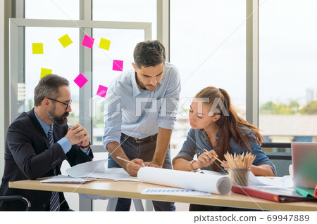 Team of multiethnic architects working on construction plans in meeting room. Engineers discussing. Team of multiethnic architects working on construction plans in meeting room. Engineers discussing. 69947889