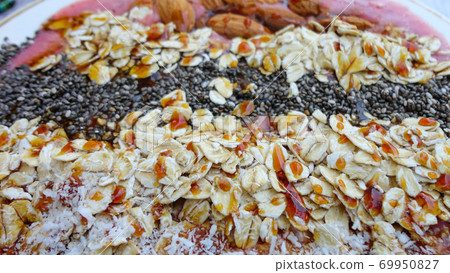 Vegan smoothie bowls with coconut flakes, chia seeds, almond and granola on pink background. Breakfast bowl with fruit and cereal, close-up, top view, healthy vegan food Vegan smoothie bowls with coconut flakes, chia seeds, almond and granola on pink background. Breakfast bowl with fruit and cereal, close-up, top view, healthy vegan food 69950827