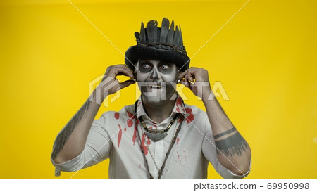 Sinister man with horrible Halloween skeleton makeup puts on headphones, starts dancing, celebrating Sinister man with horrible Halloween skeleton makeup puts on headphones, starts dancing, celebrating 69950998