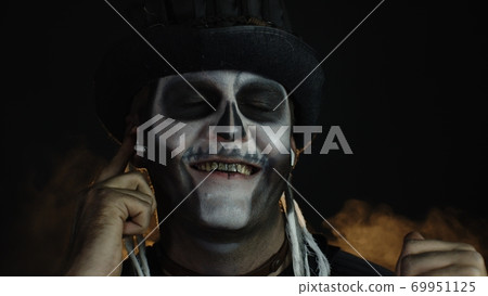 Sinister man with horrible Halloween skeleton makeup puts on headphones, starts dancing, celebrating Sinister man with horrible Halloween skeleton makeup puts on headphones, starts dancing, celebrating 69951125