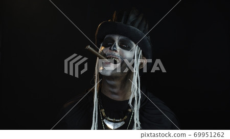 Frightening man in skeleton Halloween cosplay costume smoking cigar, making faces, smiling 69951262