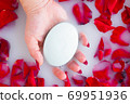 Female hand hold soap against the background of milk or white water with rose petals 69951936