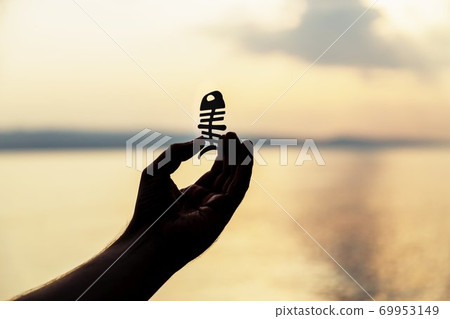 A male hand holds a fish chopsticks helper on the sea background. Sunset, silhouette. Copy space A male hand holds a fish chopsticks helper on the sea background. Sunset, silhouette. Copy space 69953149