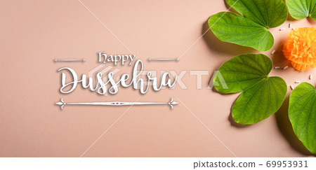 Happy Dussehra. Yellow flowers, green leaf and rice on orange pastel background. Dussehra Indian Festival concept. Happy Dussehra. Yellow flowers, green leaf and rice on orange pastel background. Dussehra Indian Festival concept. 69953931