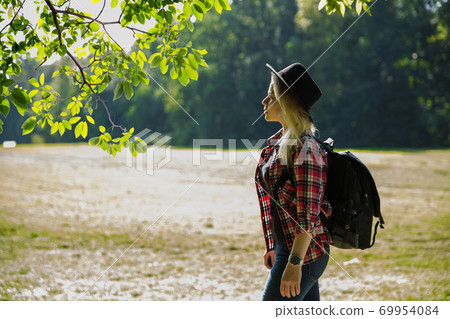 young caucasian woman with a backpack and hat near the field. young caucasian woman with a backpack and hat near the field. 69954084