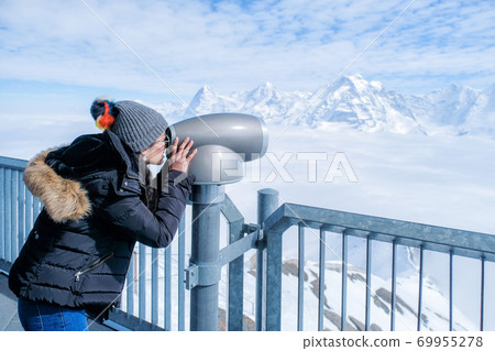 Young Woman using coin operated binocular to enjoy the panoramic view of the Swiss Skyline. Young Woman using coin operated binocular to enjoy the panoramic view of the Swiss Skyline. 69955278