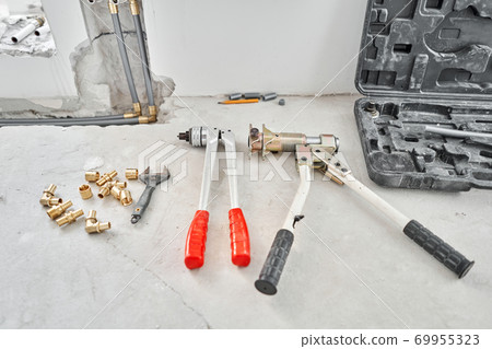 Tools for Work As A Plumber. Connection heating pipes to white Radiator in a new apartment under construction. water heating radiator on the white wall indoors Tools for Work As A Plumber. Connection heating pipes to white Radiator in a new apartment under construction. water heating radiator on the white wall indoors 69955323