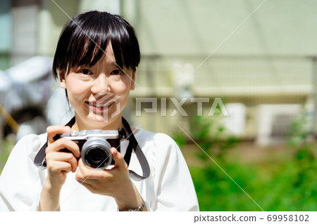 Young woman holding a camera outdoors 69958102