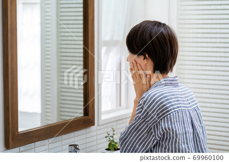 一個女人在鏡子裡檢查她的皮膚狀況。 一個女人在鏡子裡檢查她的皮膚狀況。 69960100